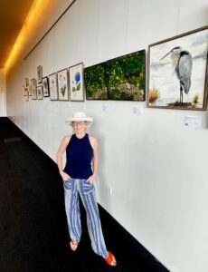 Maureen C. Berry artist author and podcaster stands alongside her nature art exhibition.